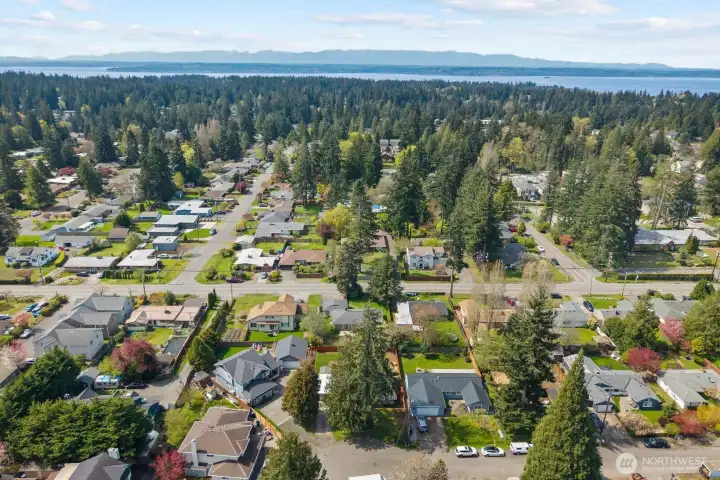 Aerial views of the property and surrounding neighborhood showcase the fully fenced backyard, open lawn, garden beds, and detached storage structure. Elevated perspectives highlight the home's residential setting, mature trees, and generous outdoor space within the established community.
