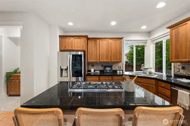 Large kitchen with cared-for cabinetry, granite countertops, stainless appliances, gas range with downdraft, tiled backsplash and dreamy corner kitchen sink area. The island comfortably seats 4-5 in addition to the eat-in dining area adjoining the kitchen. The kitchen is well-lit. Gleaming hardwood flooring.