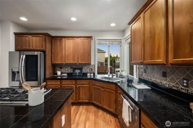 Large kitchen with cared-for cabinetry, granite countertops, stainless appliances, gas range with downdraft, tiled backsplash and dreamy corner kitchen sink area. The island comfortably seats 4-5 in addition to the eat-in dining area adjoining the kitchen. The kitchen is well-lit. Gleaming hardwood flooring.