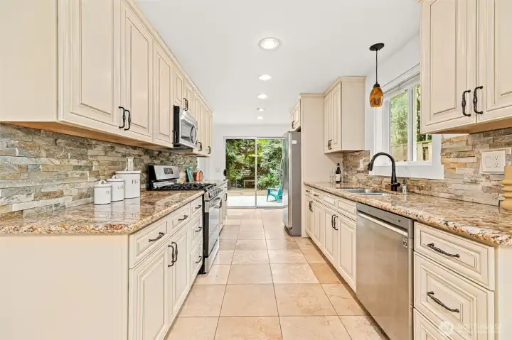 Kitchen with large tile floors and granite countertops and natural stone backsplash.