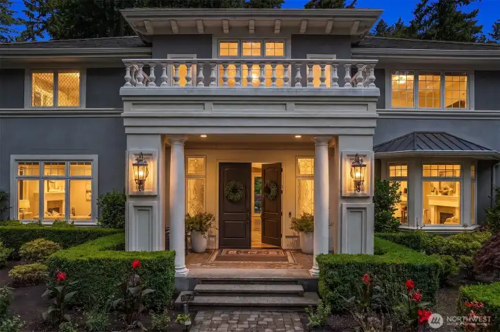 A closer look at the grand pillared portico and double-door entry porch. Accented by stone masonry pillars, stately coach lighting, and flawlessly manicured hedges that highlight the Mediterranean architectural influence