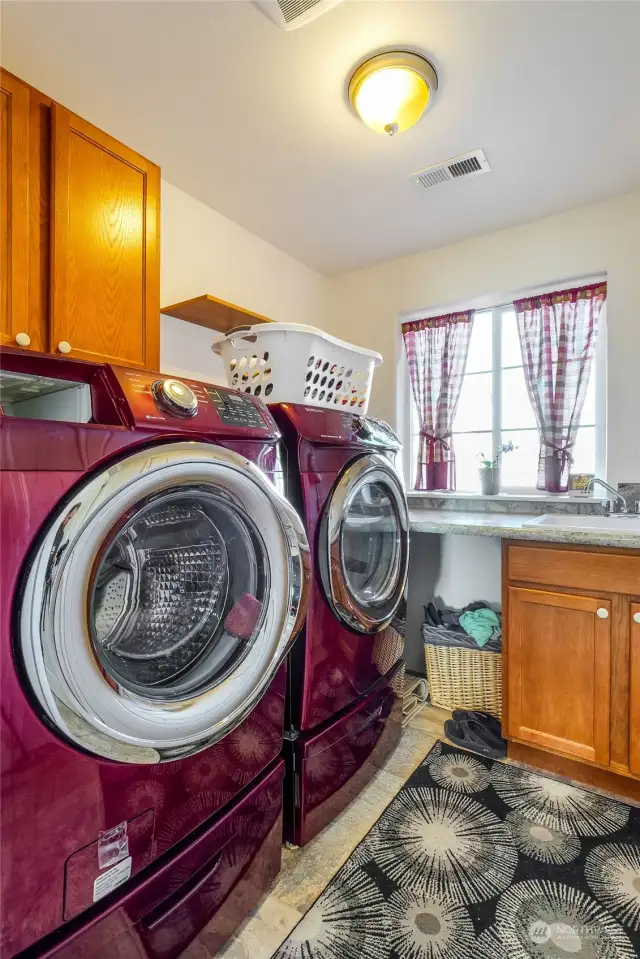 The large laundry/utility room has plenty of space for folding clothes and includes shelving and cupboards, plus a deep utility sink. Garage is to the right.