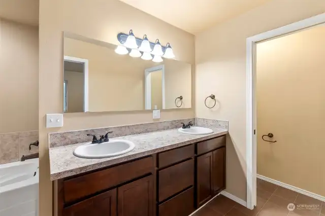 Primary bathroom with dual vanity sink, bathtub, step in shower, and private commode.