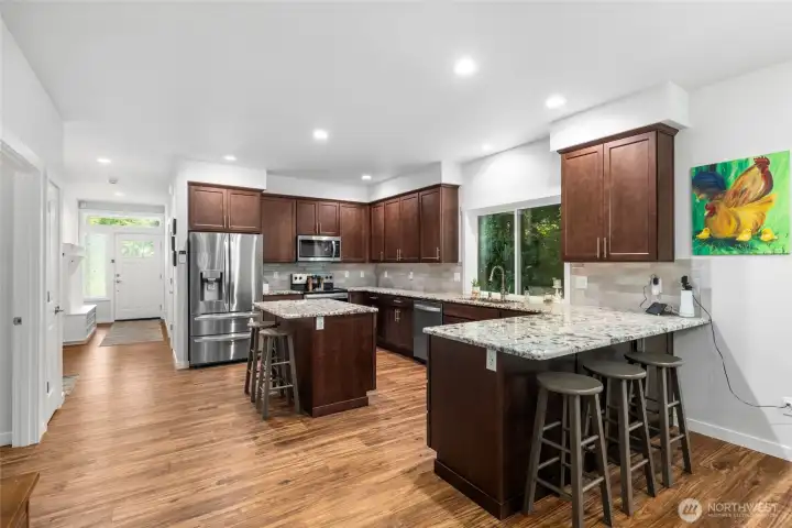 The thoughtfully designed kitchen features maple cabinetry, slab granite countertops, a full-height tile backsplash, stainless steel appliances, and durable luxury vinyl plank flooring The thoughtfully designed kitchen features maple cabinetry, slab granite countertops, a full-height tile backsplash, stainless steel appliances, and durable luxury vinyl plank flooring