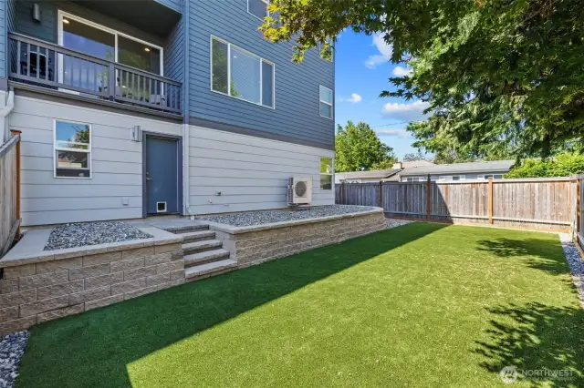 Upgraded backyard with pavers, retaining wall, rocks, turf, and a gate.