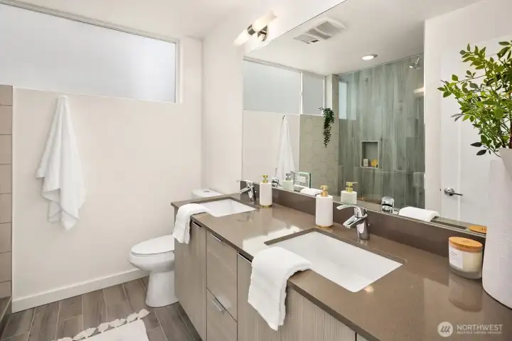 A contemporary primary 3/4 bath offers dual sinks, stone accents and a dramatic mirrored wall that enhances light and space.