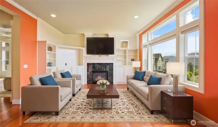 Sunlit family room featuring gleaming hardwood floors, custom built-in shelving, and a cozy gas fireplace for ultimate comfort. *Virtually Staged*