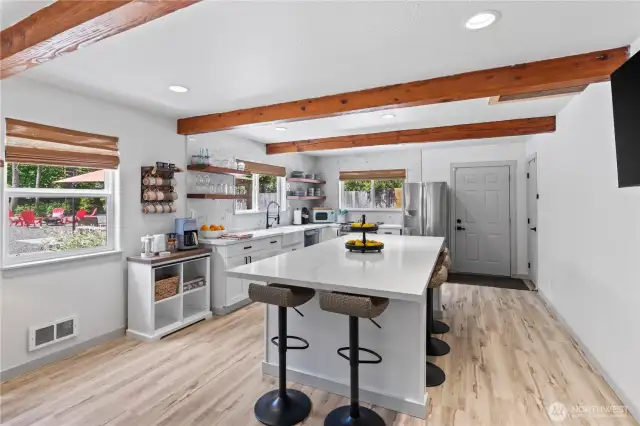 This bright and airy kitchen brings the outdoors in with two large windows framing views of the backyard patio and fire pit. The open layout features a spacious quartz island with bar seating, exposed wood ceiling beams, and a custom coffee station. Whether you're hosting guests or sipping your morning brew, this space is designed for daily enjoyment.