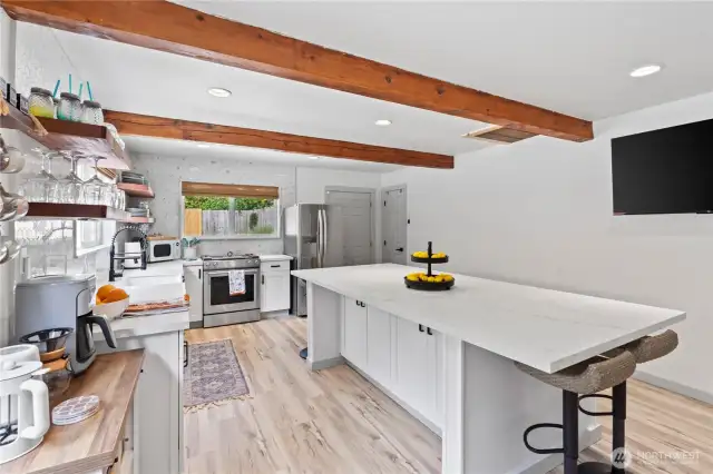 This wide-angle view captures the spaciousness of the kitchen, emphasizing the large center island perfect for meal prep or entertaining. The minimalist aesthetic is enhanced by bright quartz counters, shaker-style cabinetry, and seamless access to the living space. This kitchen effortlessly combines beauty with functionality.