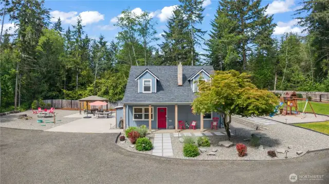 This crisp daytime shot showcases the home's inviting front exterior with fresh landscaping, a covered porch, and a bold red door that makes a memorable first impression. The expansive, well-designed backyard includes a patio with gazebo, fire pit seating area, and dedicated playground space—all beautifully laid out and easy to maintain. Ideal for families, entertainers, or those seeking tranquility with modern comforts.