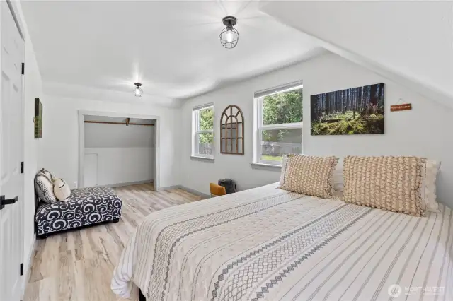 This serene upstairs bedroom features soft natural light, cozy sloped ceilings, and a spacious layout with room for both rest and relaxation. The dual windows overlook the lush backyard, while the open closet nook adds practical storage potential. Light wood flooring and neutral tones make this space feel bright and inviting.
