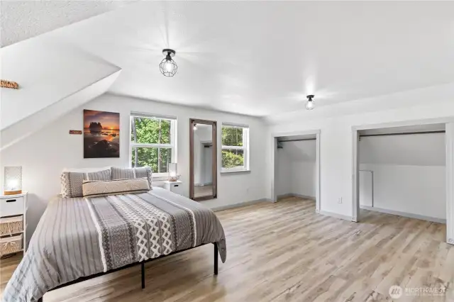 A continuation of the spacious layout, this angle shows the full depth of the bedroom, with symmetrical closet space and soft wood flooring. Natural light flows through the double windows, enhancing the calming color palette and cozy comfort of the room.