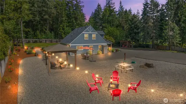 Step into your dream backyard oasis, where string lights set the mood and the warmth of a fire pit invites you to unwind. This twilight view captures the home’s spacious patio, covered gazebo with seating, and multiple entertainment zones—from outdoor dining to late-night s’mores. Surrounded by privacy fencing and tall evergreens, it’s the ultimate setting for gatherings or peaceful evenings under the stars.