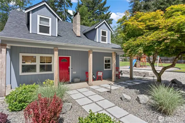 This inviting front entry blends rustic charm with modern updates. A vibrant red door, warm wood columns, and fresh landscaping welcome you home. The stone path adds elegance and functionality, while the nearby tree and view of the playground space highlight the home’s family-friendly design and thoughtful outdoor planning.