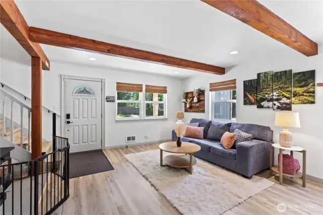 Step into a bright, welcoming living room filled with warmth and personality. From the white entry door with decorative glass to the cozy couch setup and rustic wood accents on the wall, this space is both stylish and functional. Ample windows provide natural light and views of the private yard, creating a perfect blend of indoors and outdoors.