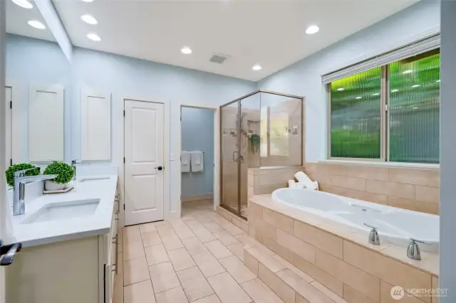 The roomy primary en suite bathroom with radiant floor heating. Double sinks and beautiful quartz countertops. Textured glass window allows the light in while maintaining privacy.  Linen closet is center with the separate toilet room to the right for added privacy.