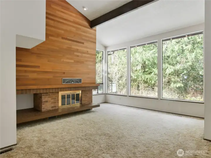 Living room features Pacific NW lodge aesthetic: Vaulted ceilings, exposed beams, large wall windows & wood buring firplace.