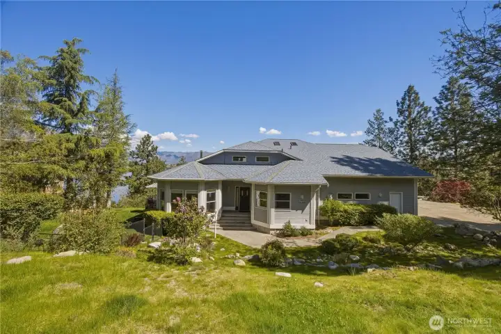 Surrounded by mature trees and lush green landscaping. A well-maintained lawn and natural vegetation frame the house, creating a private, peaceful setting.