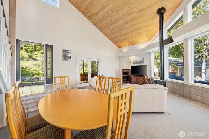 Dining area with a round wood table and chairs, set beside large windows that bring in natural light and outdoor views.