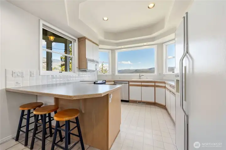 Bright kitchen with white cabinetry, ample counter space, and eating bar. Large windows wrap the space, filling it with natural light and offering epic lake views.