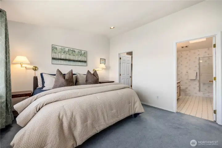 Primary bedroom with neutral tones, large windows, and soft natural light. Features a spacious layout, wood furnishings, and direct access to the ensuite bath.