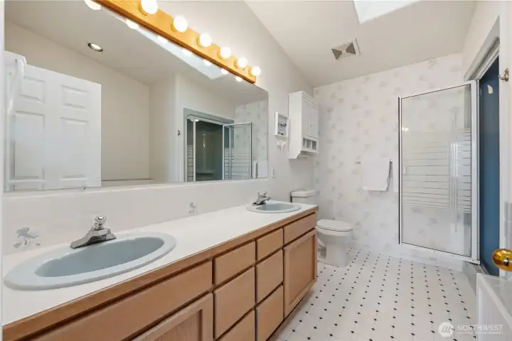 Primary bathroom with dual-sink vanity, wood cabinetry, and large mirror with overhead lighting. Features a enclosed shower, soaking tub, and bright, spacious layout.