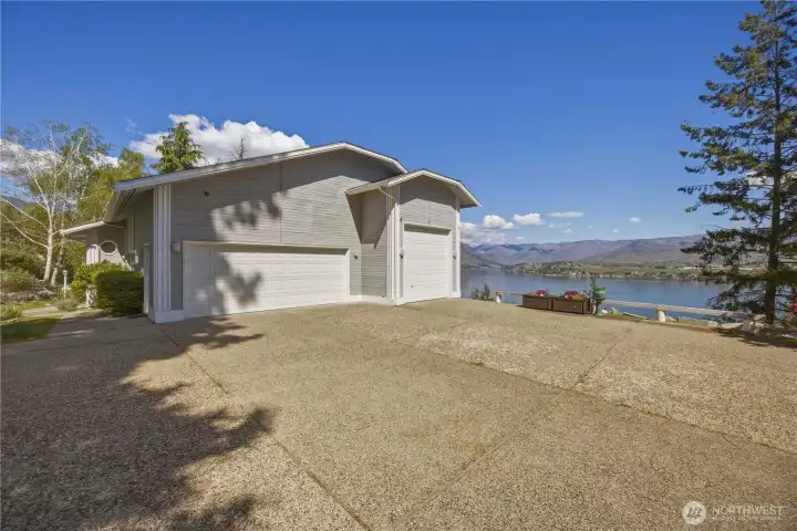 Driveway and front exterior with ample parking space, leading to a home with an attached garage. Positioned to capture elevated lake and mountain views in a bright, open setting.