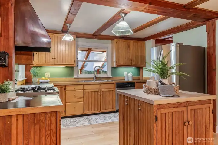 Kitchen with propane stove, island, marble cutting board, dishwasher, stainless steel refrigerator, and plenty of storage.