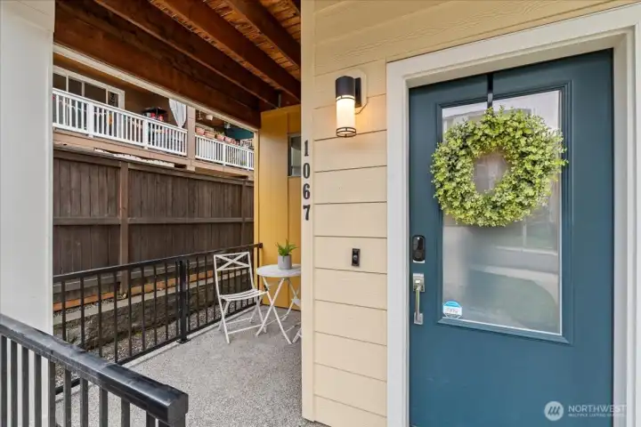 Front Porch detail with outdoor seating space, overhead cover, and modern entry door with decorative accent. Ideal for a small seating or relaxation area.