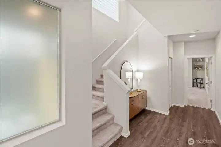 Foyer and staircase with modern railing, and adjacent console space. Bright interior with natural and overhead lighting.
