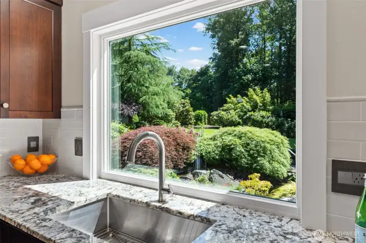 A showpiece kitchen window brings the outdoors in, offering a stunning view of the lush landscaping and water feature while filling the prep area with natural light.