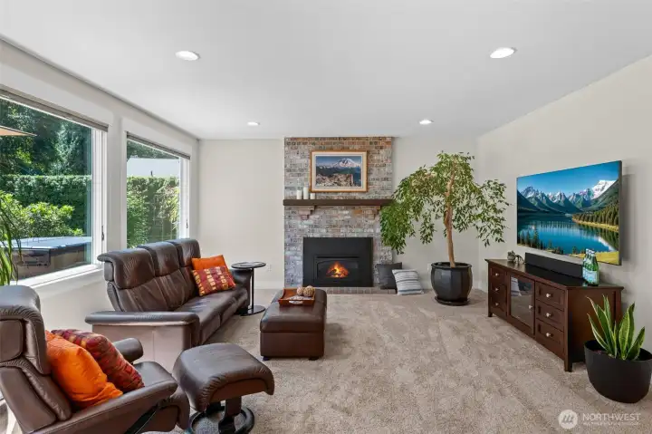 The family room features a floor-to-ceiling brick fireplace with a gas insert, plush carpet, and oversized windows framing mature greenery just outside.