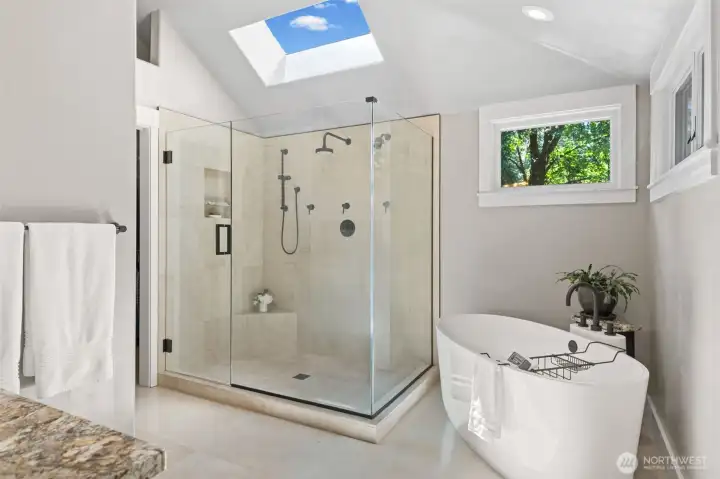 The beautifully updated Primary Bath features a frameless glass shower with heated travertine tile, a rain shower head, and a skylight that fills the space with natural light. There's a freestanding soaking tub and a wall of tall windows that frame the tree-lined views. Don't miss the spa-inspired atmosphere, perfect for unwinding after a long day.
