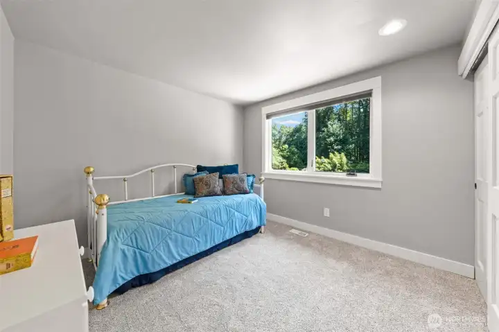Bedroom 2 features plush carpet, blinds, a wide window framing tree-lined views, and a closet for everyday storage. Don't miss the bright, versatile layout, ideal as a guest room, kids' room, or creative space.
