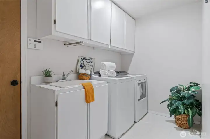 The utility room features a built-in sink, ample overhead storage, and space for full-size washer and dryer, keeping everyday chores organized and out of sight. Notice the door to the left that leads to the garage.