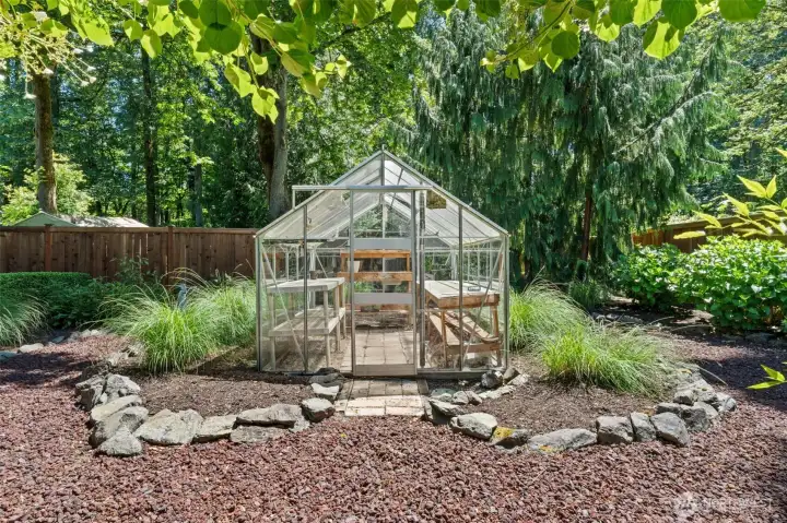 A private greenhouse with built-in potting benches, nestled among ornamental grasses and a rock-edged garden bed along the cedar fence line await you here. Perfect for all your garden needs!