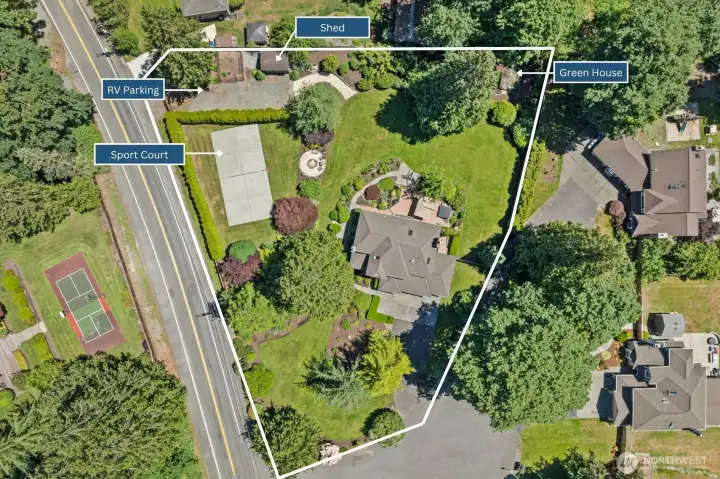 This aerial view reveals an expansive, beautifully landscaped lot featuring a sports court, fire pit patio, and spacious Trex deck off the back of the home, all surrounded by mature trees for ultimate privacy. The gated RV parking area off to the side adds rare functionality, offering plenty of room for vehicles, toys, or storage on this exceptional home.