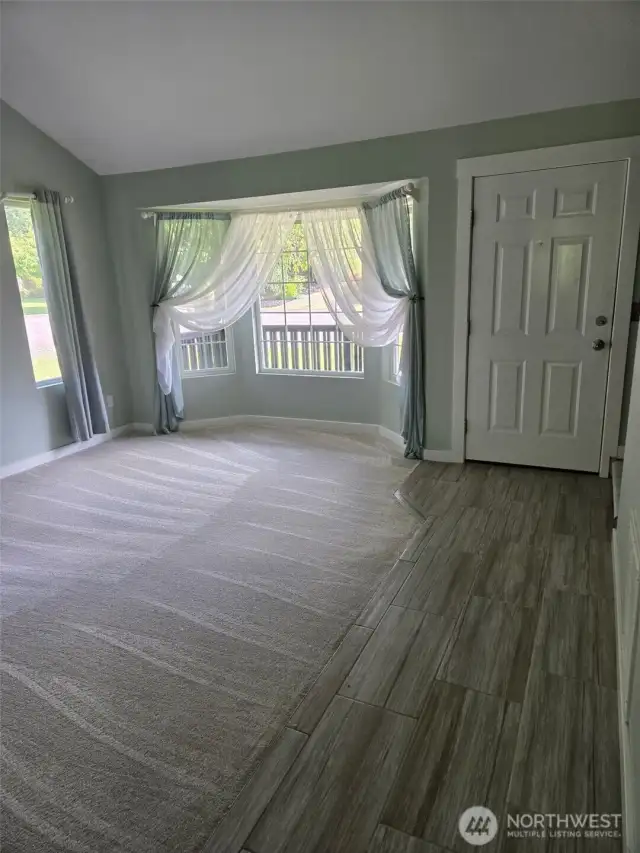 Natural light pours into this formal living room through a large bay window with charming sheer drapes. Plush carpet and luxury tile flooring create a welcoming and stylish first impression.