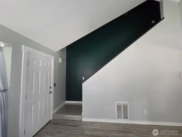 Modern entryway with striking vaulted ceilings and a bold accent wall along the stairwell. Tile flooring flows into the main living area, adding a clean, contemporary touch to the home's layout.
