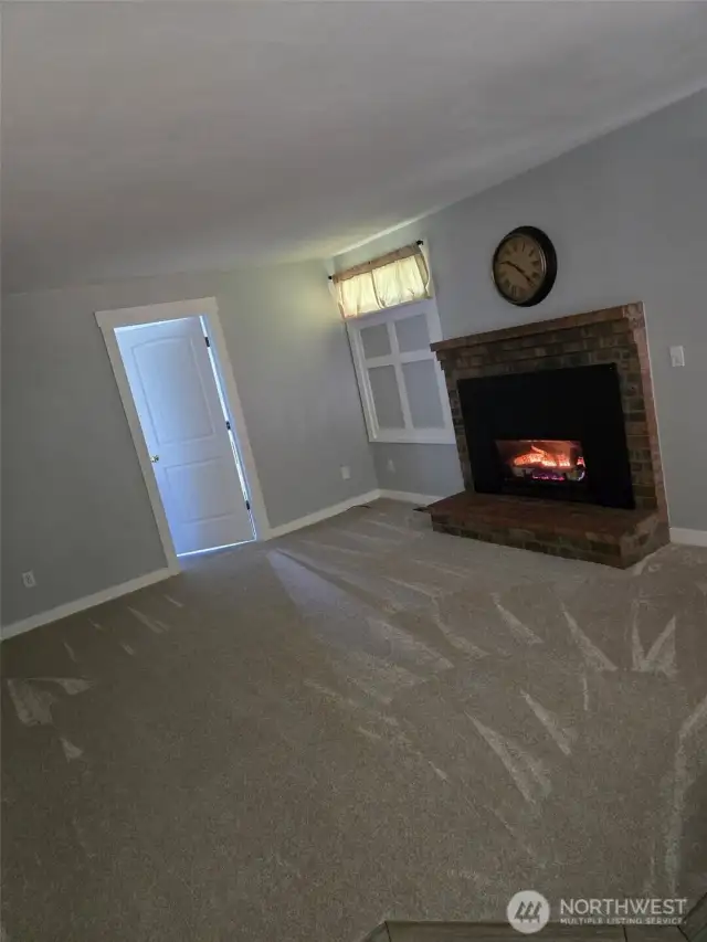 The cozy living room invites you in with fresh carpet, a warm gas fireplace, and neutral paint throughout. A charming wood mantel and soft natural light create an inviting setting for gatherings.