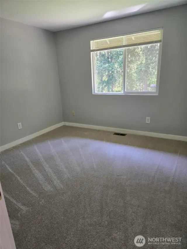 This clean and quiet upstairs bedroom features fresh carpet and a large window overlooking lush trees. It's a comfortable space for winding down or setting up a private study area.