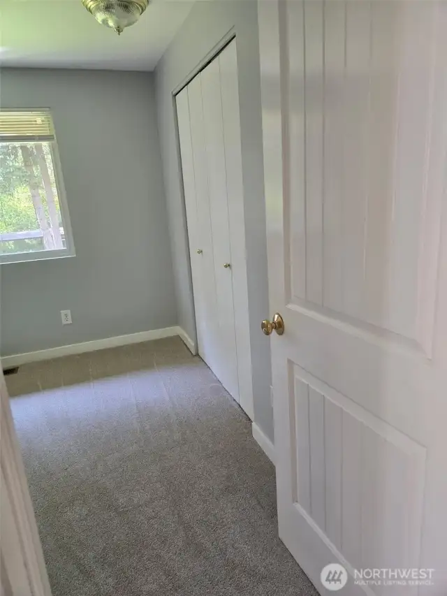 Natural light floods this secondary bedroom, which includes a large closet and a peaceful view of the surrounding evergreens. The soft gray walls and white trim offer a fresh, modern aesthetic.