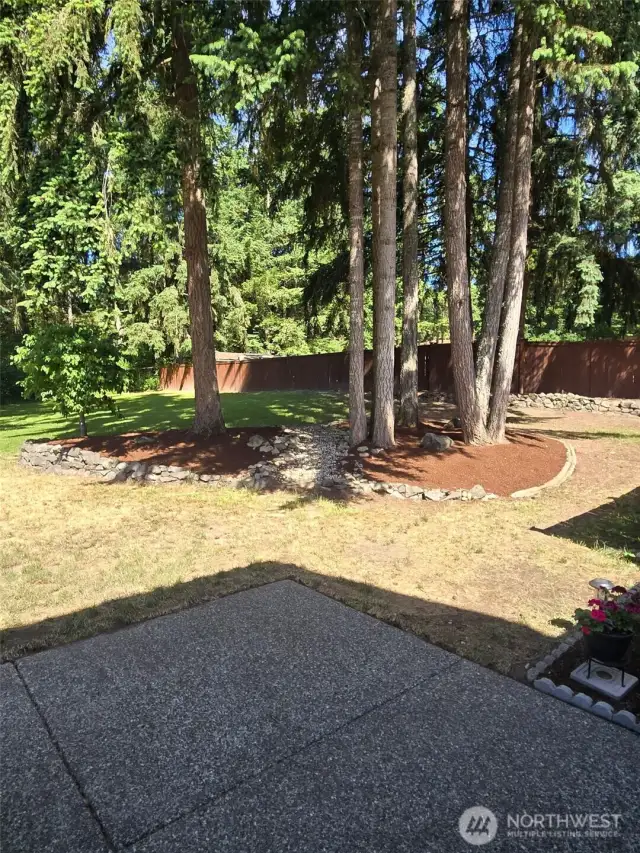 Step out back to a tranquil yard framed by mature evergreens. This beautifully landscaped corner features river rock edging and bark mulch, providing a serene spot to relax or create your own woodland garden.