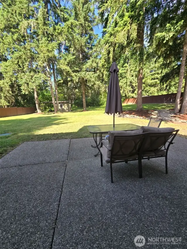 Kick back in your private forest retreat. This patio setup invites cozy conversations under the canopy of Northwest evergreens, with room to expand your outdoor living space.