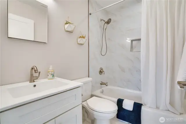 Fresh from top to bottom—tile floors, sleek vanity, updated fixtures, tile surround with bath accessory niche, and modern lighting create a spa-worthy main floor bathroom.