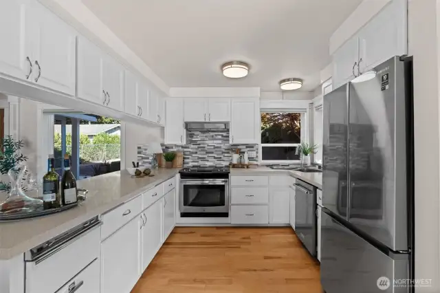A modern kitchen with quartz countertops, stainless steel appliances, and crisp white cabinetry.
