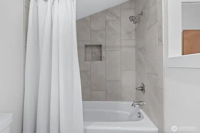 A well-appointed guest bath with hard surfaces and a tile-lined shower.