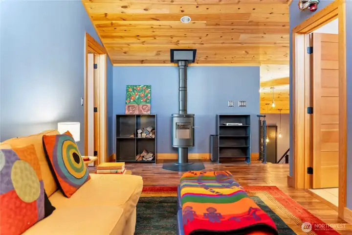 The living room has warm wood ceilings, a Morso stove, and custom steel firewood storage cabinets.