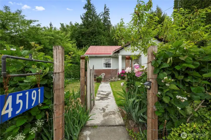 Charming garden gate opening into lush landscaping featuring seasonal blooming peonies.