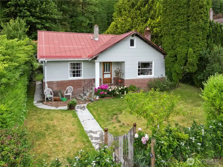 Newer metal roof cottage framed by a fully fenced front yard and gated entry.